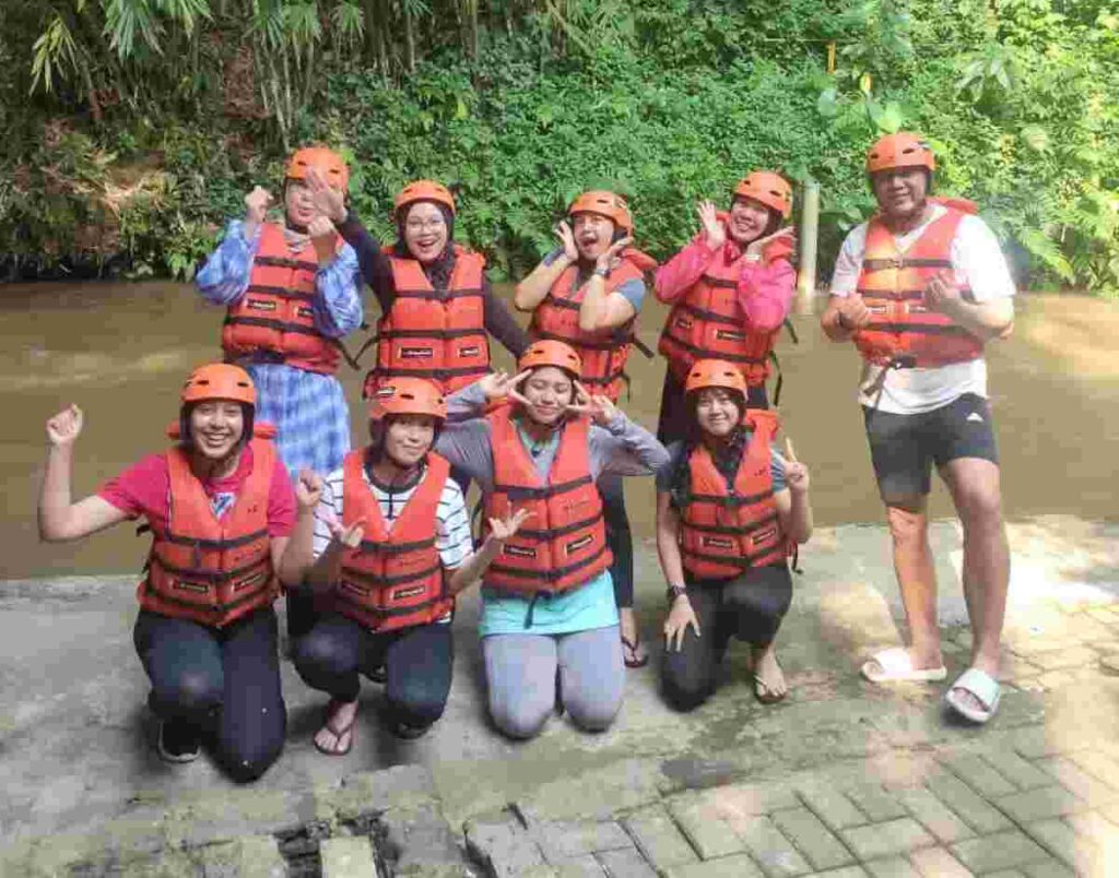 Karyawan perusahaan mengenakan helm pelindung sedang tersenyum ceria saat mengikuti kegiatan outbound team building di Sentul